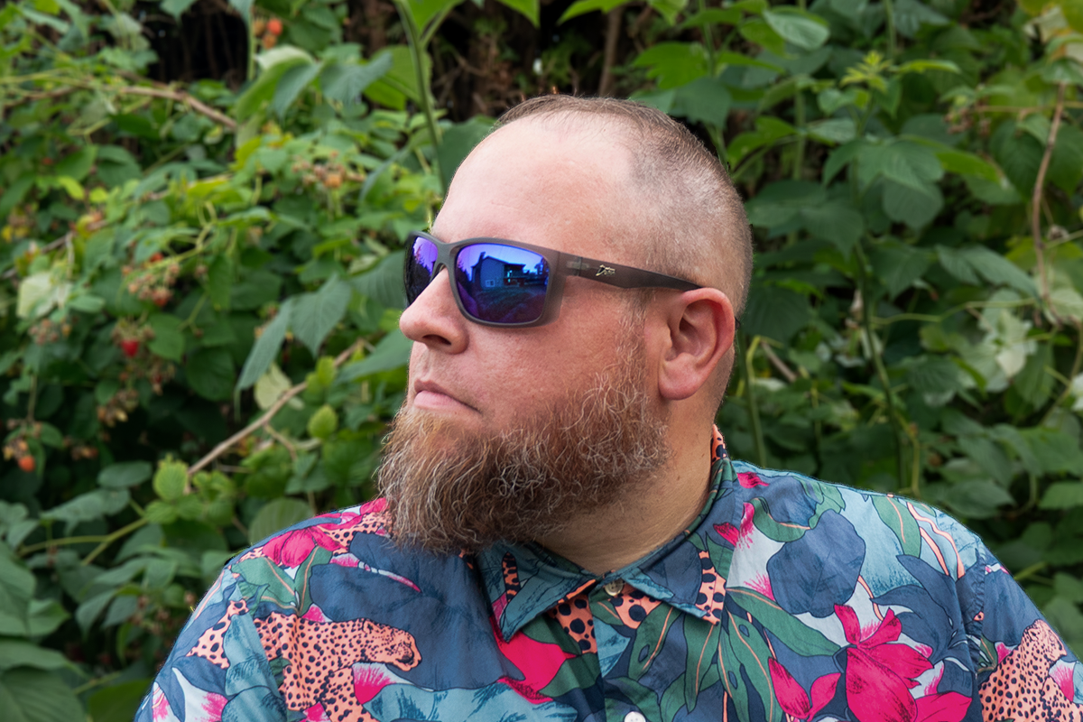 Man wearing mirrored goggles and gray beanie, holding skis in a snowy setting.
