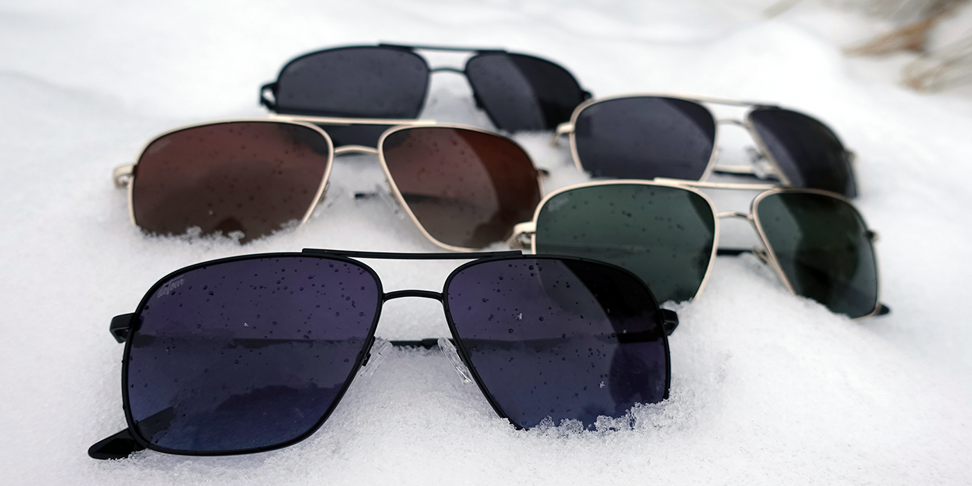 Man wearing mirrored goggles and gray beanie, holding skis in a snowy setting.