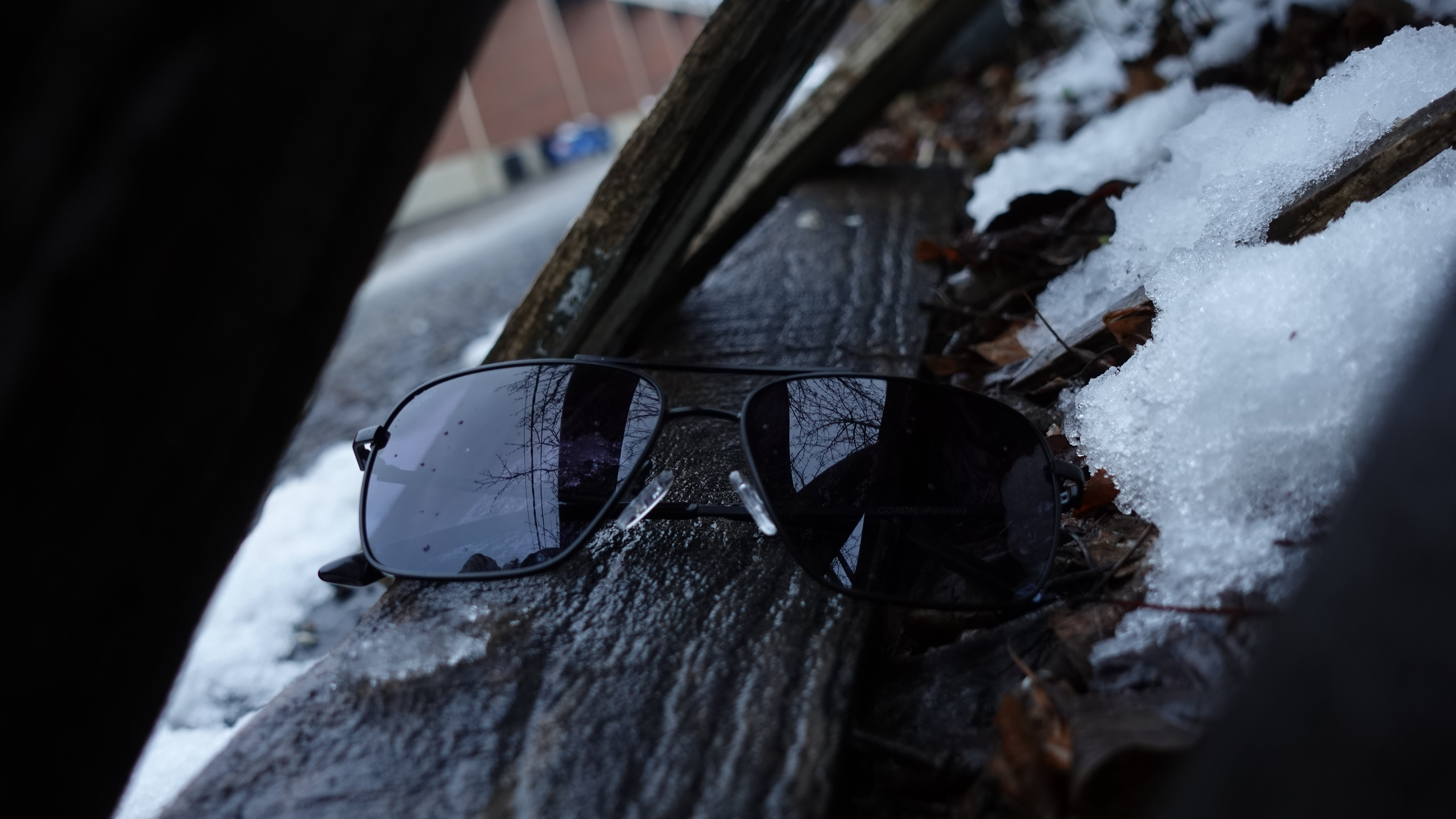 Man wearing mirrored goggles and gray beanie, holding skis in a snowy setting.