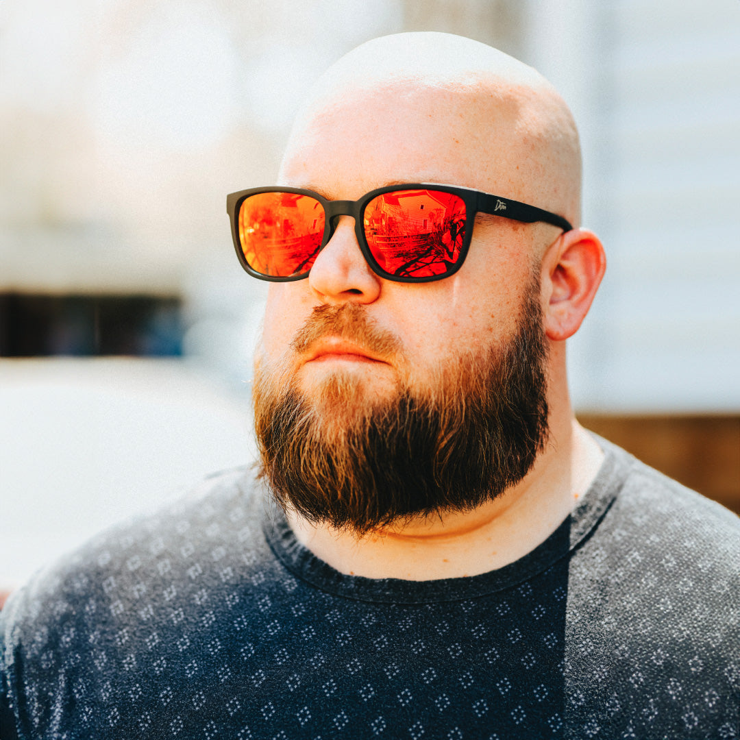 Man wearing mirrored goggles and gray beanie, holding skis in a snowy setting.