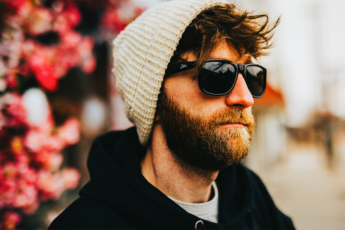 Man wearing mirrored goggles and gray beanie, holding skis in a snowy setting.