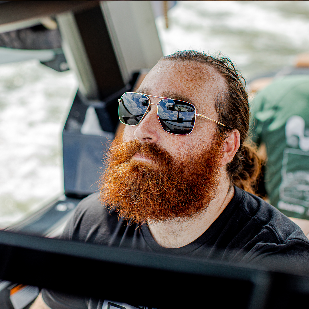 Man wearing mirrored goggles and gray beanie, holding skis in a snowy setting.