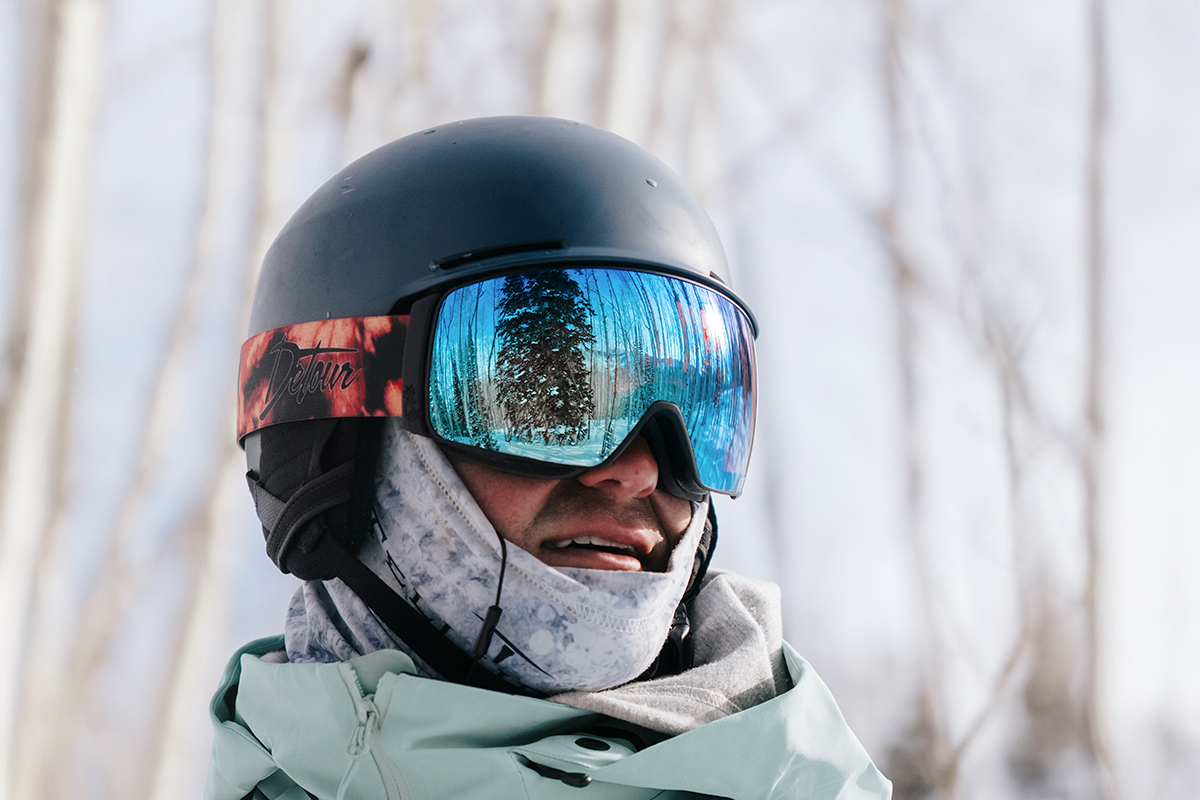 Person holding purple ski goggles with snowy background.